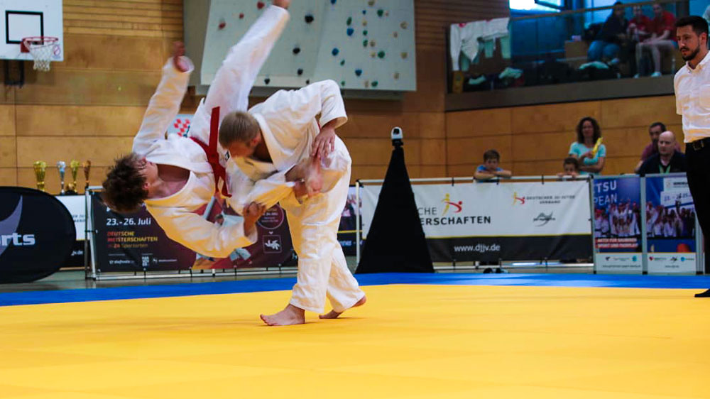 Athlet Steffen Bienias wirft Tjark Rose bei der Deutschen Meisterschaft Ju-Jutsu 2026 auf der gelben Wettkampfmatte, beide im weißen Gi mit rotem Gürtel. Ju-Jutsu DUO Training Süpplingen