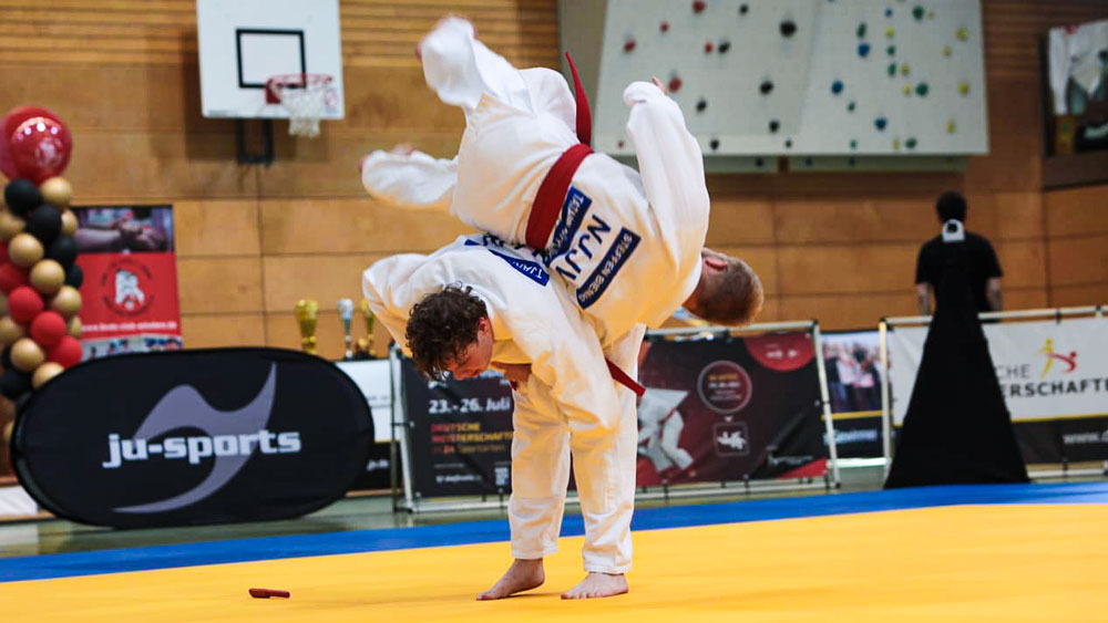 Athlet Tjark Rose wirft Steffen Bienias bei der Deutschen Meisterschaft Ju-Jutsu 2026 auf der gelben Wettkampfmatte, beide im weißen Gi mit rotem Gürtel. Ju-Jutsu DUO Training Süpplingen
